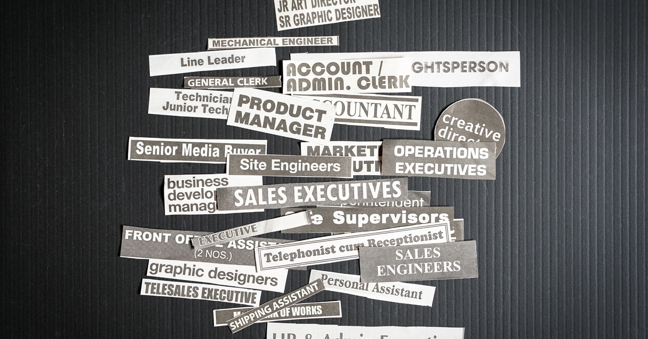 Multiple job titles or occupations cut off from newspaper on black background.