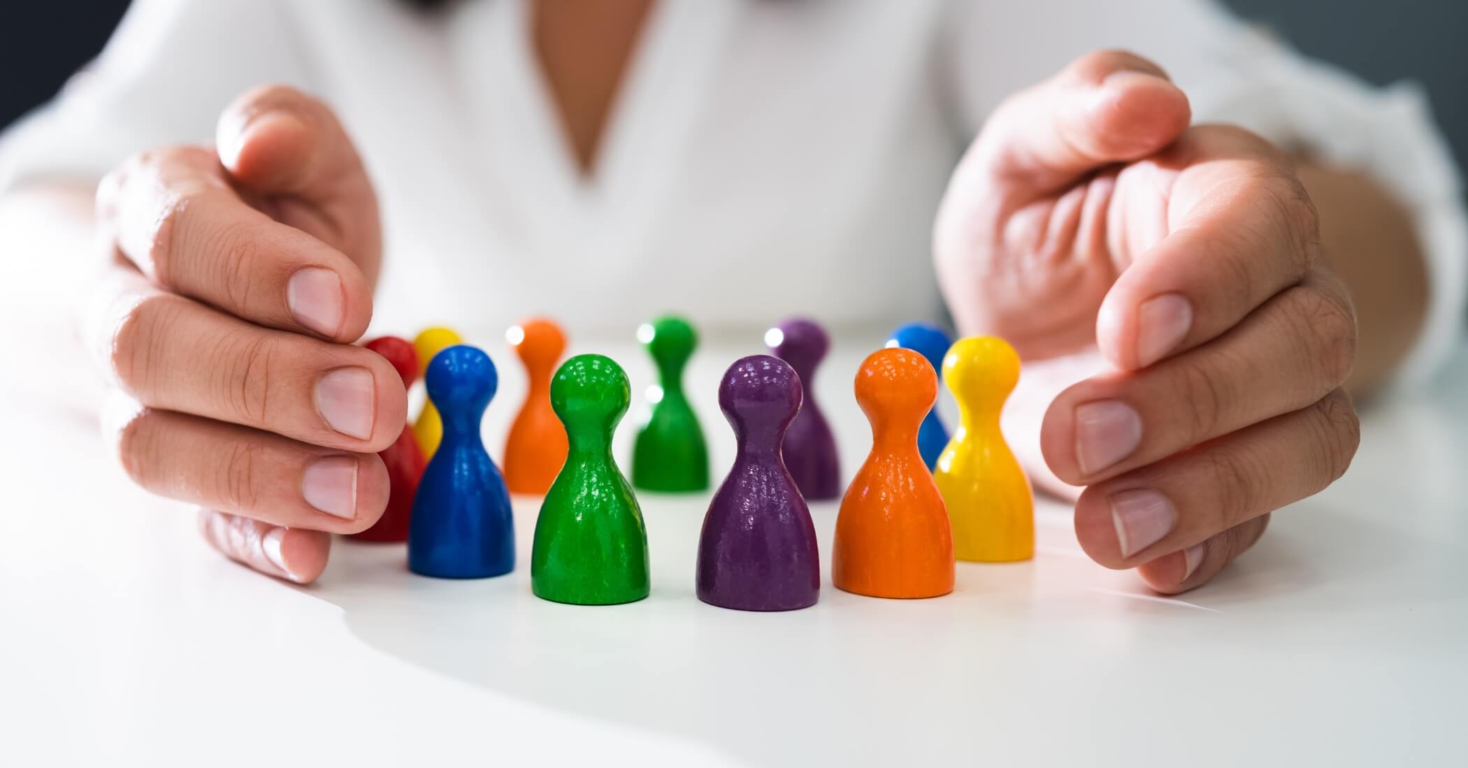 Hand protecting colourful wooden figures, inclusion, equality and diversity protection concept.